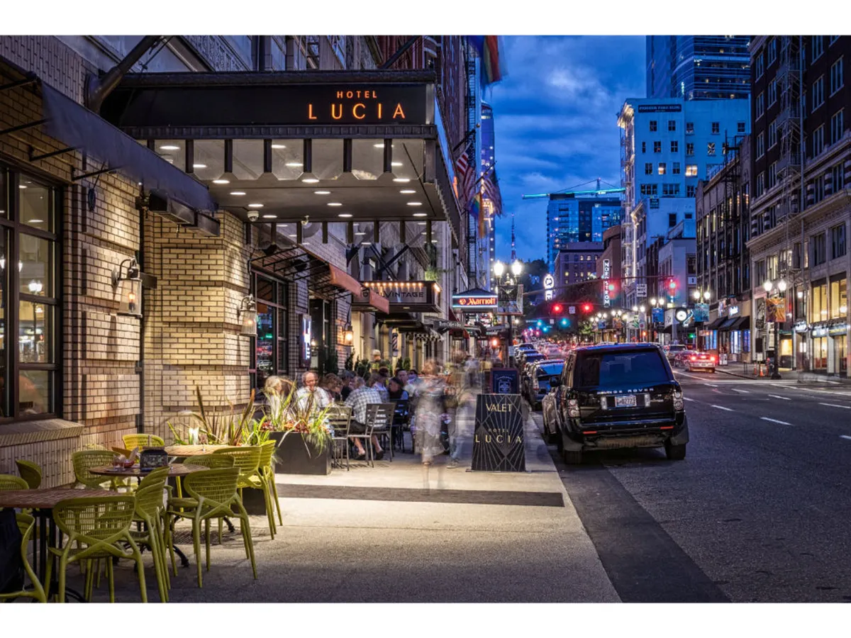 Hotel Lucia’s inviting outdoor seating area is alive with guests dining and socializing under the city’s glow. The scene is energetic and urban, highlighting the hotel's connection to Portland’s nightlife and vibrant pedestrian culture.