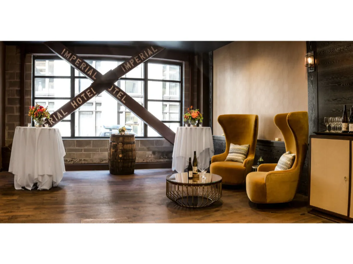 A welcoming lounge with two yellow armchairs, tables adorned with floral arrangements, a wine bottle atop a table, and a rustic barrel accent. The atmosphere is sophisticated and comfortable, ideal for unwinding or intimate conversation.