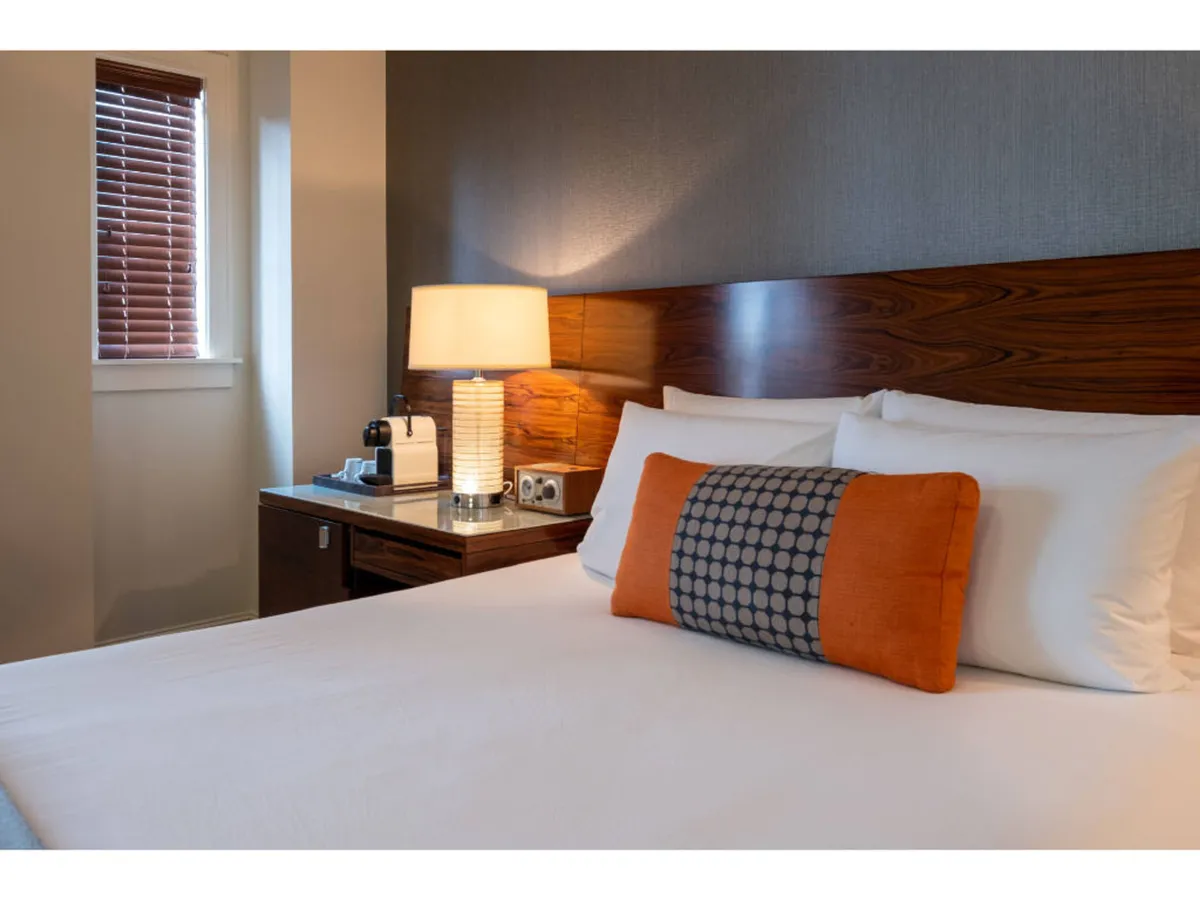 A serene guest room with a comfortable bed, decorative pillow, lamp, and nightstand, radiating a sense of relaxation and comfort. The space is well-lit and suggests an inviting place to unwind.