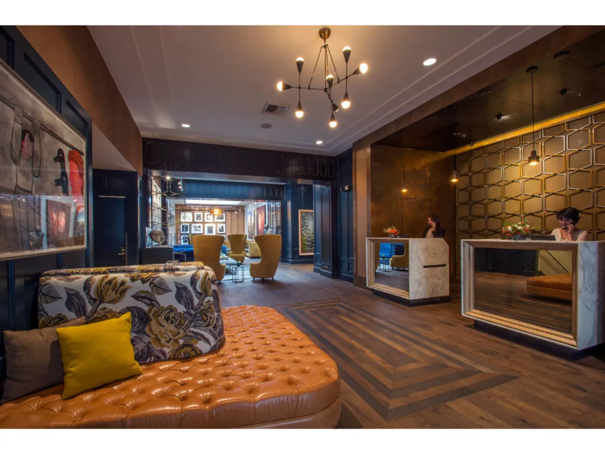 This image presents a stylish hotel lobby area featuring an ornate reception desk, vibrant contemporary artwork on the walls, and a comfortable seating arrangement. The space feels lively and welcoming, with guests potentially checking in, socializing, or relaxing over coffee.