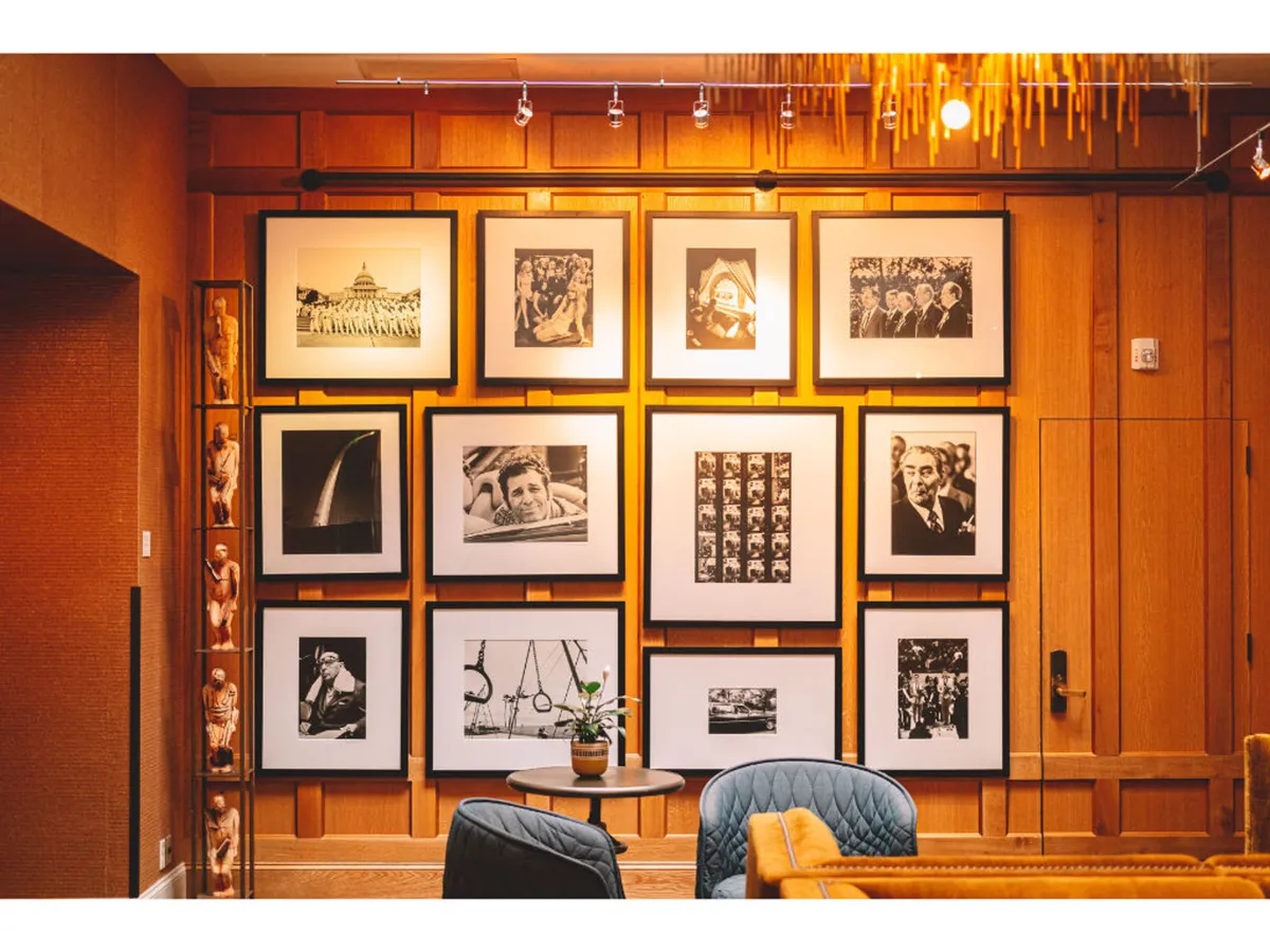 A stylish seating area set against a gallery wall of striking black-and-white photographs, with comfortable chairs and a decorative plant. The gallery wall prominently displays a curated photographic collection, inviting guests to engage in quiet conversation or contemplation while surrounded by creative inspiration.