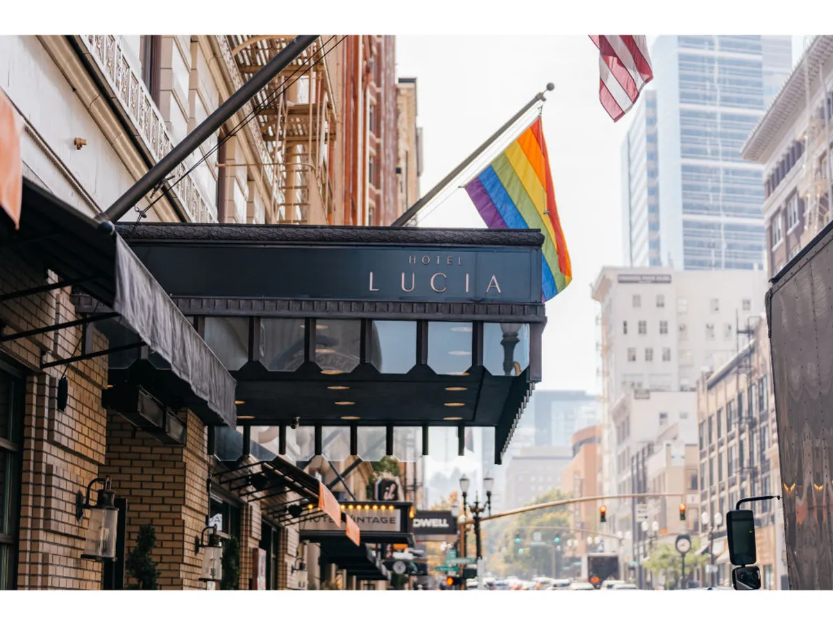 This exterior shot features the Hotel Lucia's iconic signage, proudly flanked by the rainbow and American flags. Vibrant city life unfolds just outside, inviting visitors to explore Portland's urban landscape. The image hints at nearby attractions, local culture, and the hotel's inclusive, welcoming spirit.